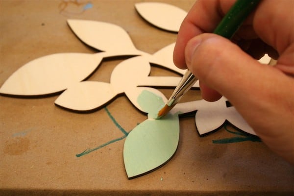 Painting a wood piece with light green craft paint using a paintbrush