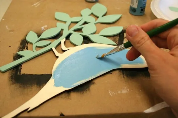 Painting a wood piece with light blue craft paint using a paintbrush