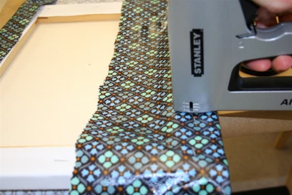 Using a staple gun to attach fabric to the back of a canvas