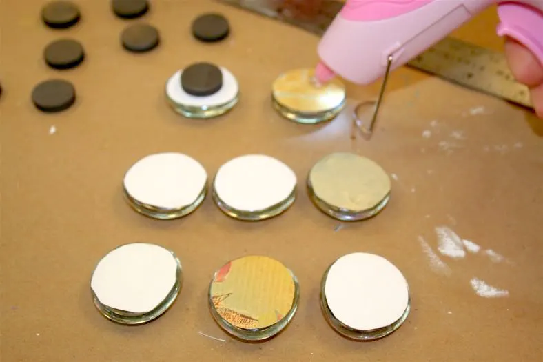 Using a hot glue gun to attach black magnets to the back of glass marbles 
