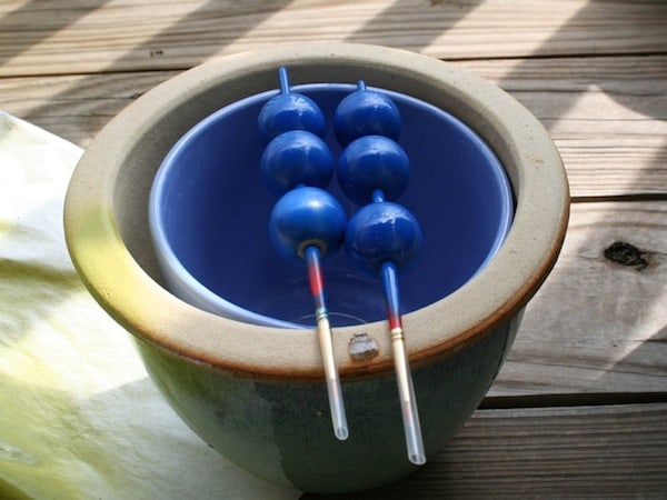 Wood balls spray painted with blue paint and drying on a clay pot