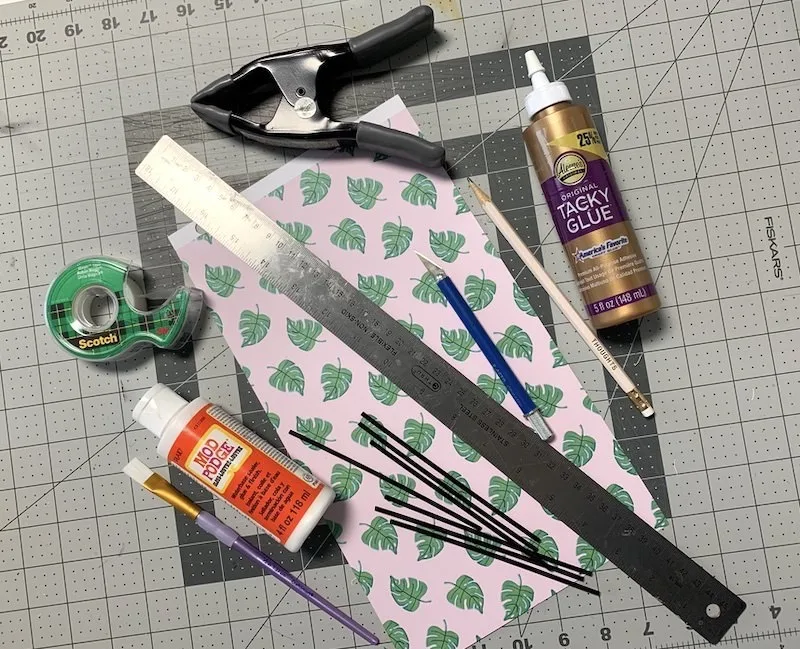 Scrapbook paper, craft glue, Mod Podge, coffee stirrers, ruler, craft knife, tape, and a pencil