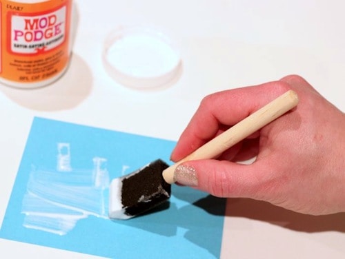 Adding Mod Podge to the blue cardstock with a foam brush