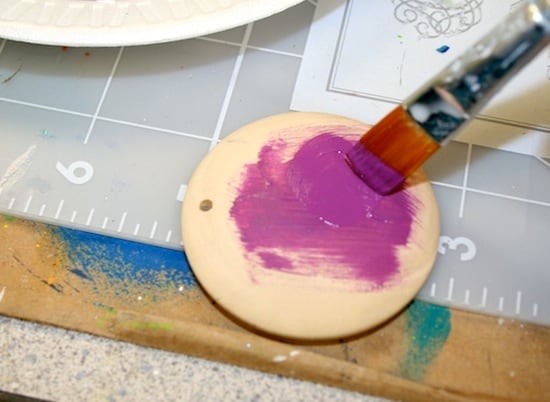 Painting the back of a wood pendant with purple acrylic paint and a paintbrush
