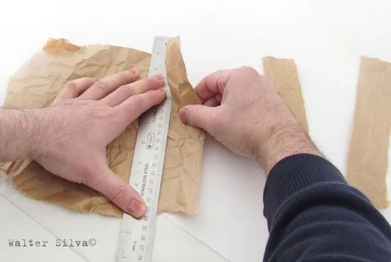 Man's hands tearing a paper bag along a ruler
