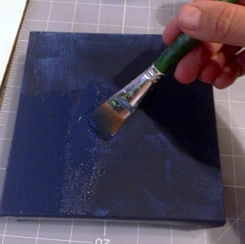 Painting a canvas with navy blue acrylic paint