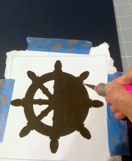 Cutting a nautical wheel silhouette out of scrapbook paper using a template and craft knife
