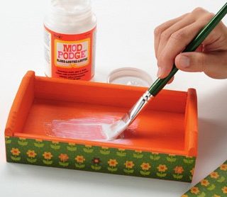 Painting Mod Podge Gloss inside of a painted wood tray with a green handled paint brush