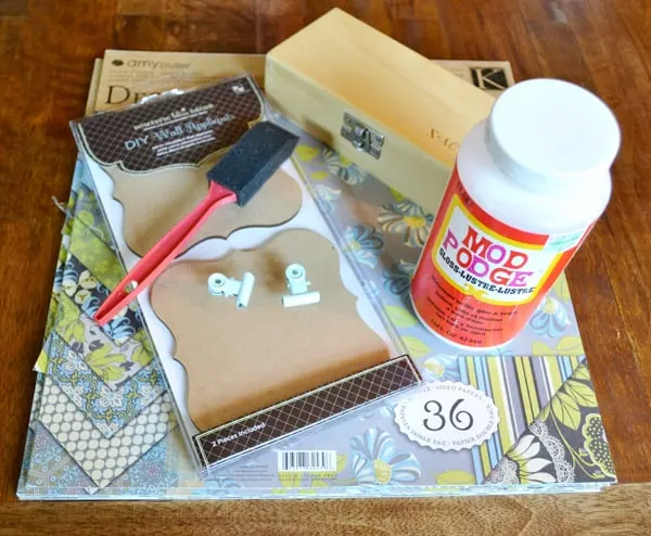 Scrapbook paper, clip frames, craft knife in a box, Mod Podge Gloss, and a foam brush