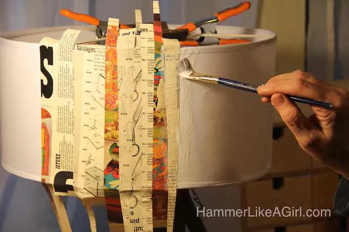Adding Mod Podge and paper strips to a lampshade with a paintbrush