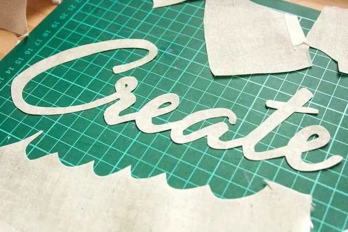 The word "create" cut from fabric laying on a cutting mat