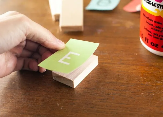 Placing a small rectangle with the letter E down on a wood block with Mod Podge