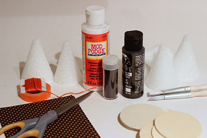Foam cones, black paint, Mod Podge Gloss, scrapbook paper, scissors, glitter, wood circles, and paintbrushes