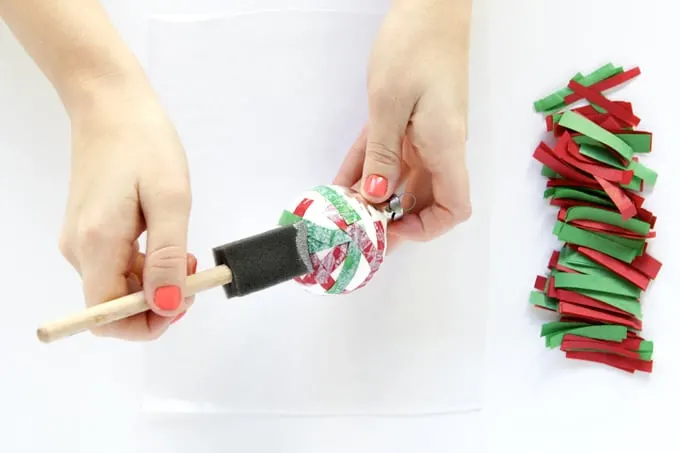 Applying a layer of Mod Podge over the top of a confetti ornament with a foam brush