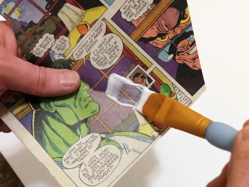 Adding Mod Podge to a comic book page with a paintbrush