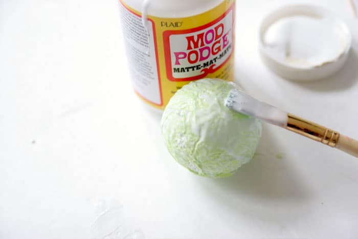 Mod Podging green tissue paper onto a styrofoam ball