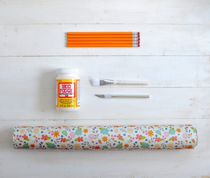 Bottle of Mod Podge, roll of floral paper, craft knife, and paintbrush
