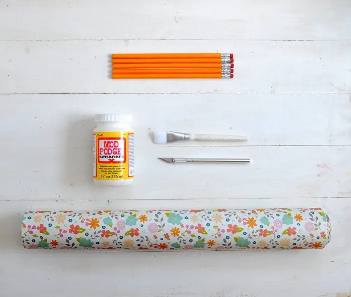 Bottle of Mod Podge, roll of floral paper, craft knife, and paintbrush