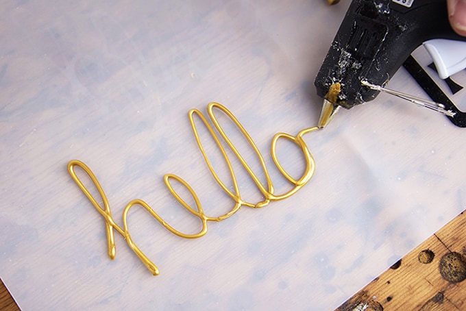 Hello written in gold hot glue on a silicone mat