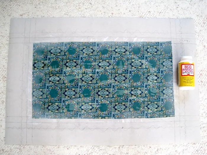 Fabric decoupaged to the back of a piece of linoleum with a Mod Podge bottle laying next to it