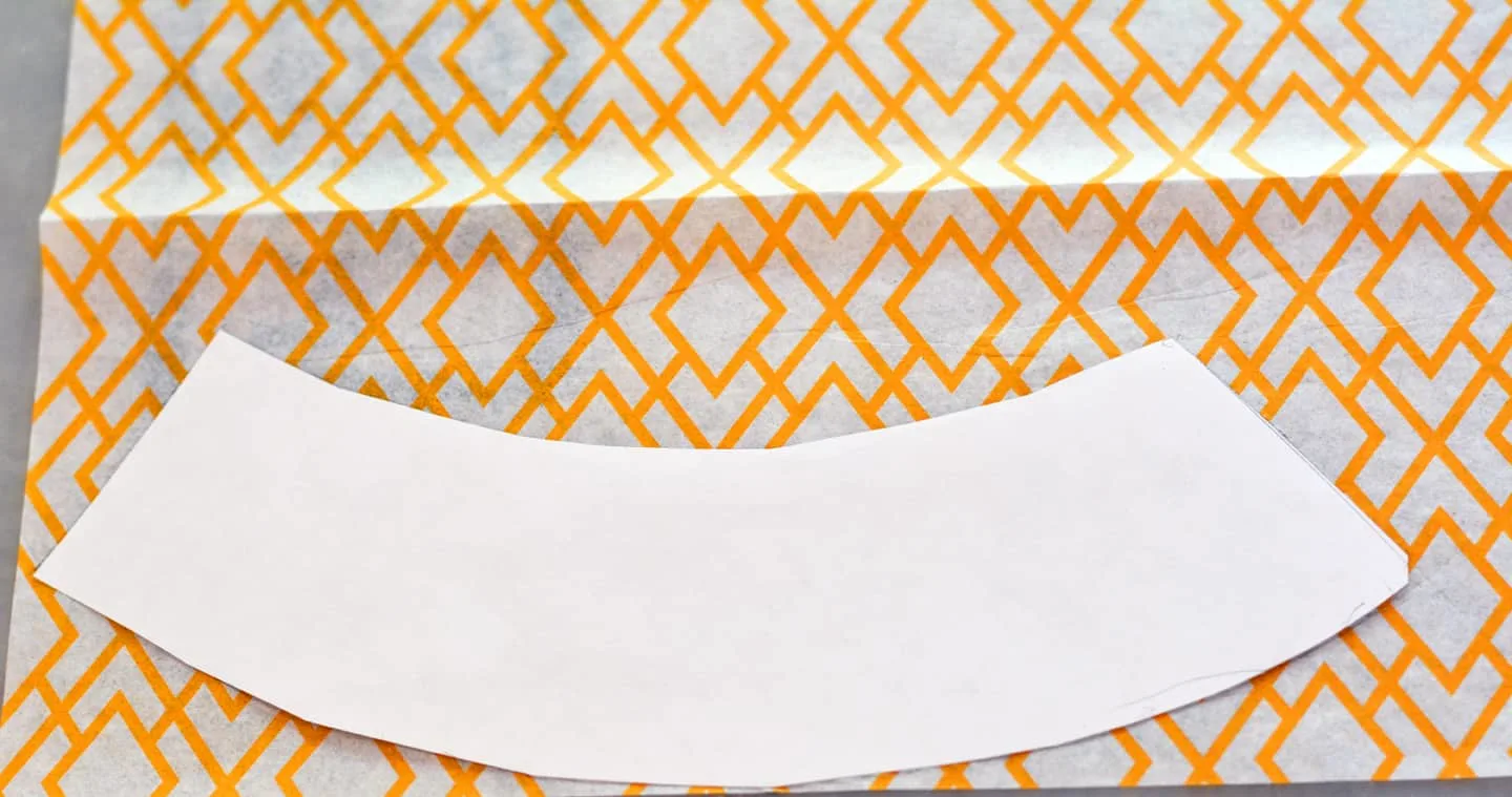 A paper pattern laid on the top of a piece of orange patterned tissue paper
