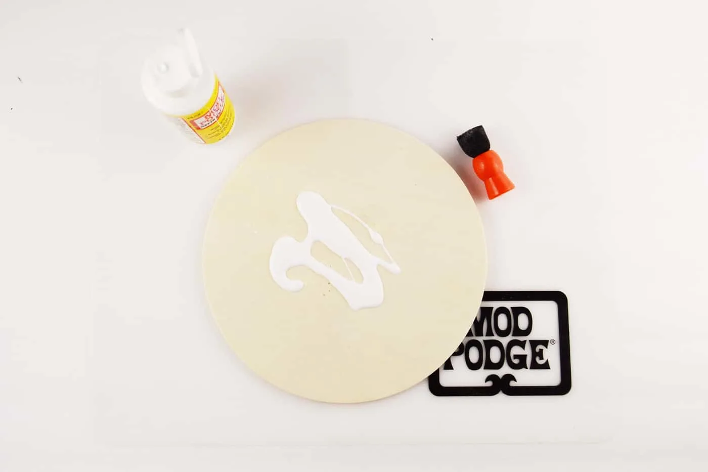 Mod Podge Matte on top of a wood circle with a spouncer next to it