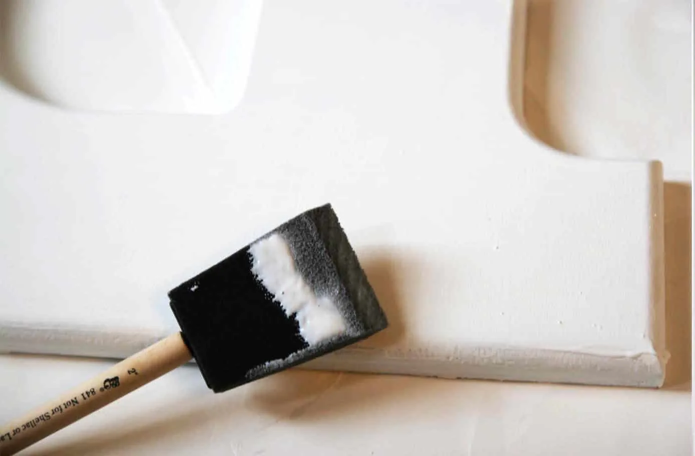 Applying Mod Podge to a white wooden letter with a foam brush