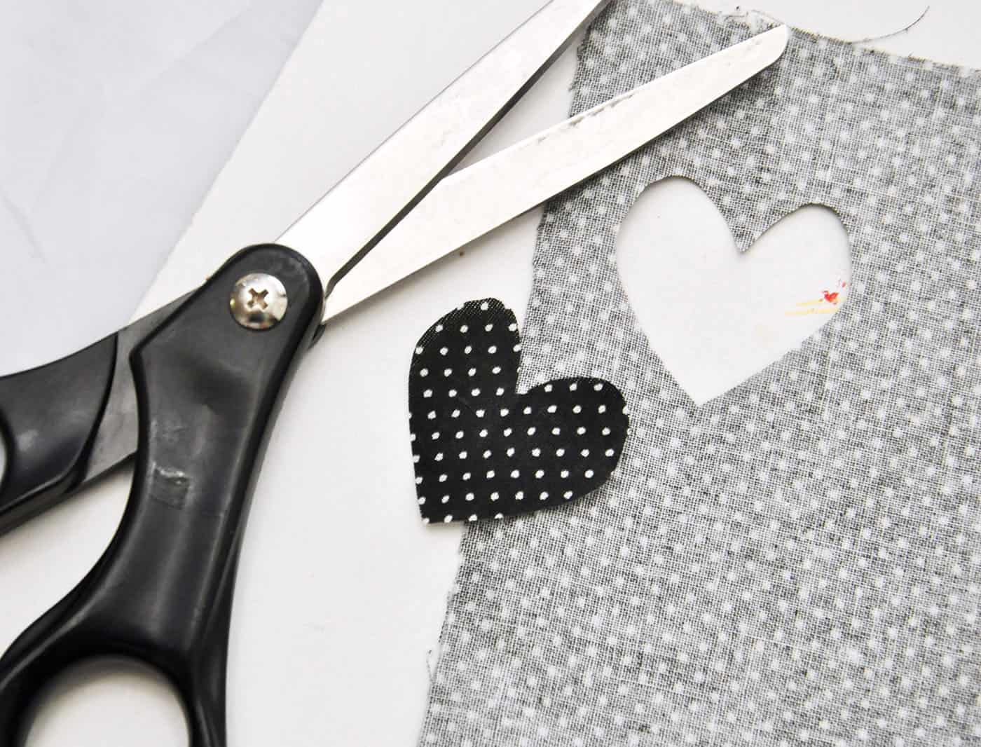 Heart cut out of black fabric with white polka dots using black handled scissors