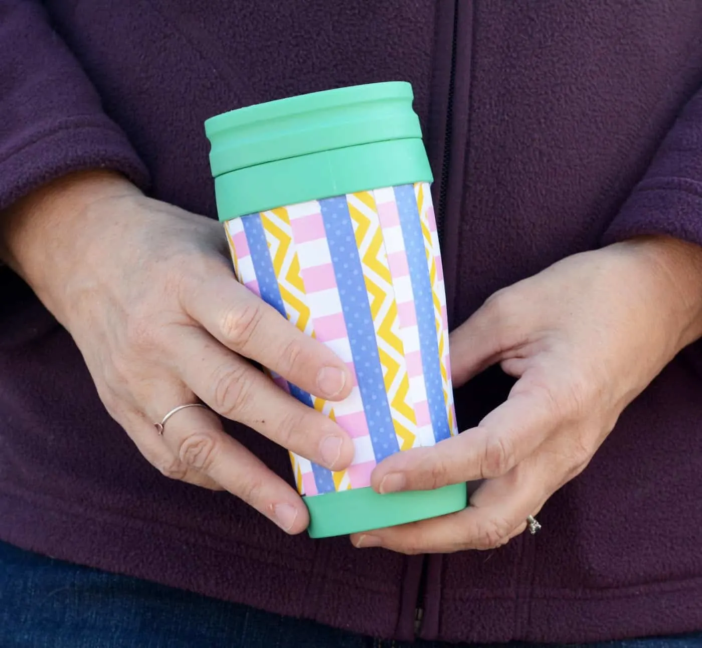 Closeup of a woman holding a decorated travel mug in front of her waist