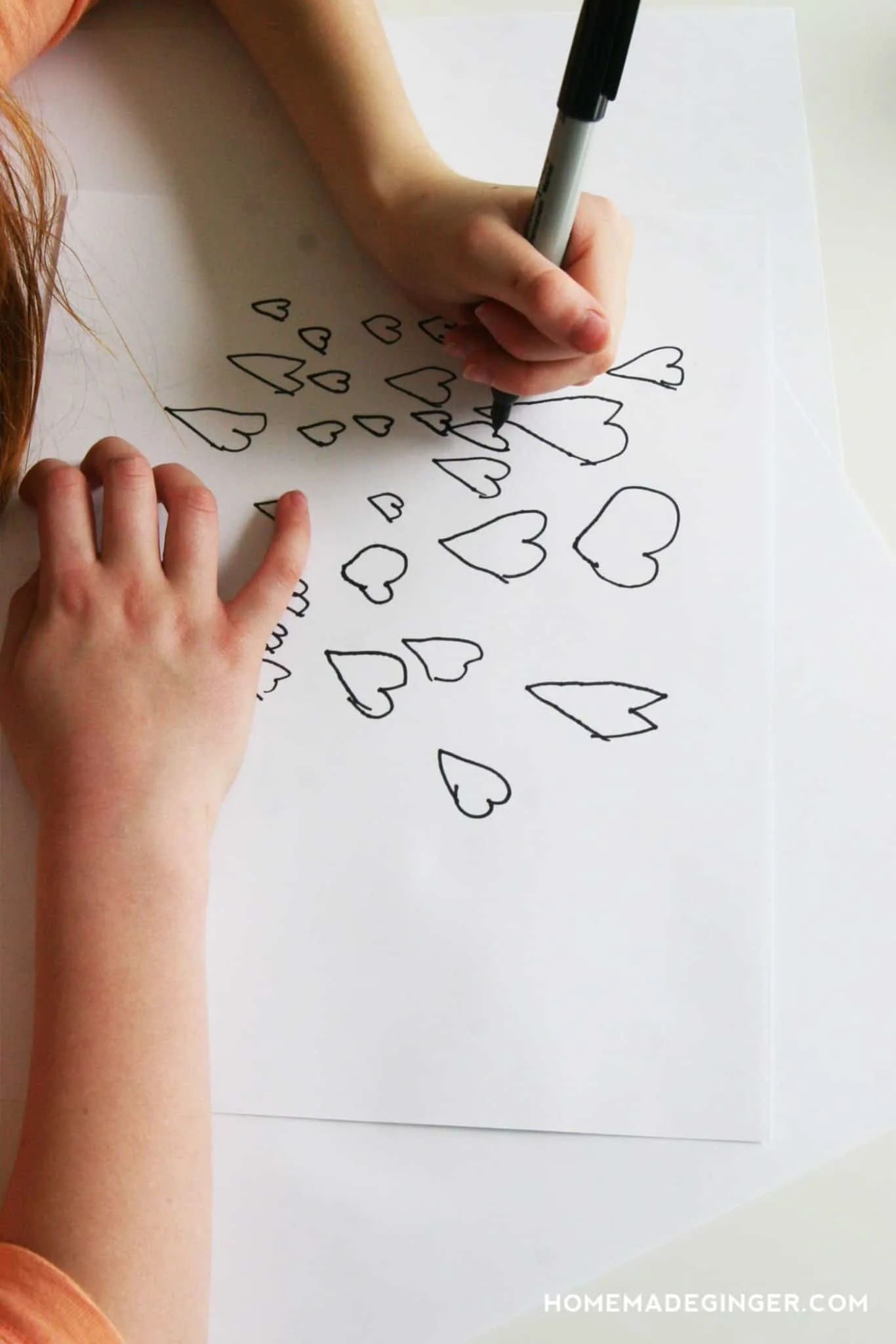 Child drawing hearts on a piece of white paper with a Sharpie