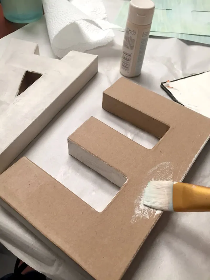 Painting the paper mache letters with warm white acrylic paint