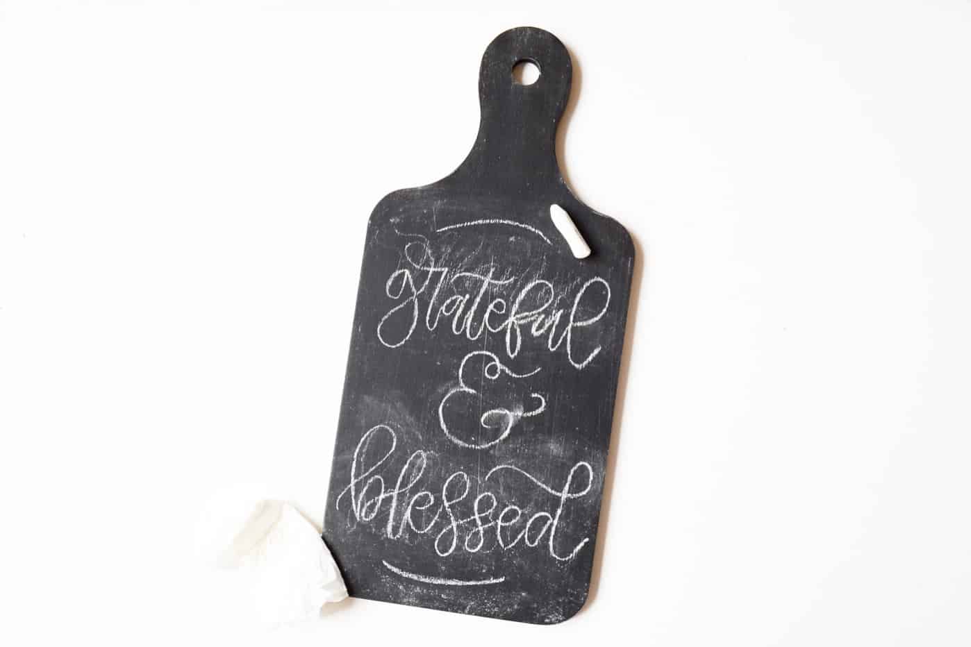 Bread board painted with black chalkboard paint that says grateful and blessed