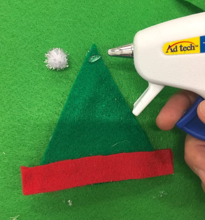 Attaching a pom pom to the top of an elf hat with hot glue