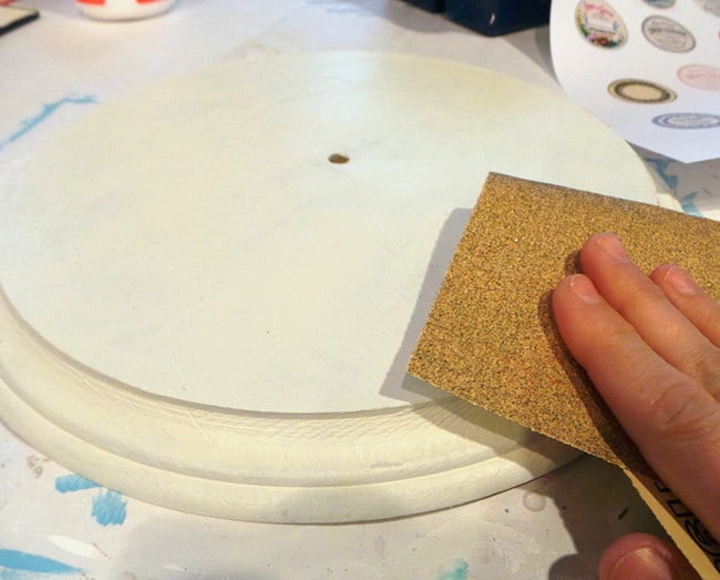 Sanding a DIY wood wall clock with sandpaper to reveal distressing