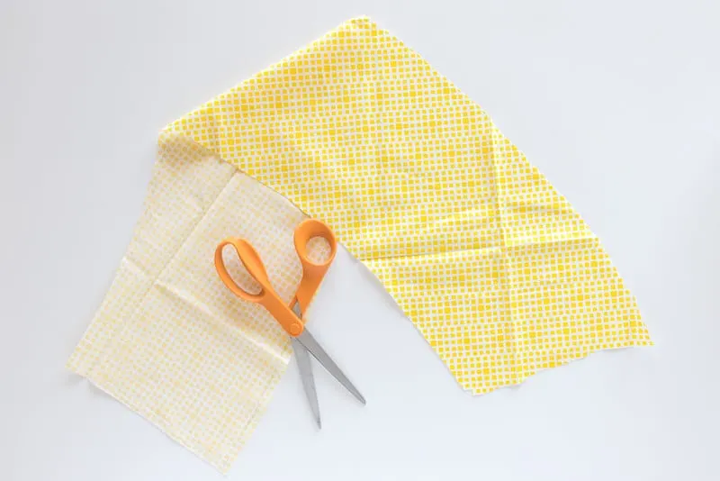 Cut out piece of fabric with orange handled scissors laying on top