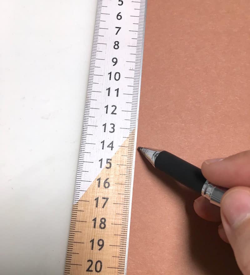 Using a ruler and a pen to draw a line on a piece of brown construction paper