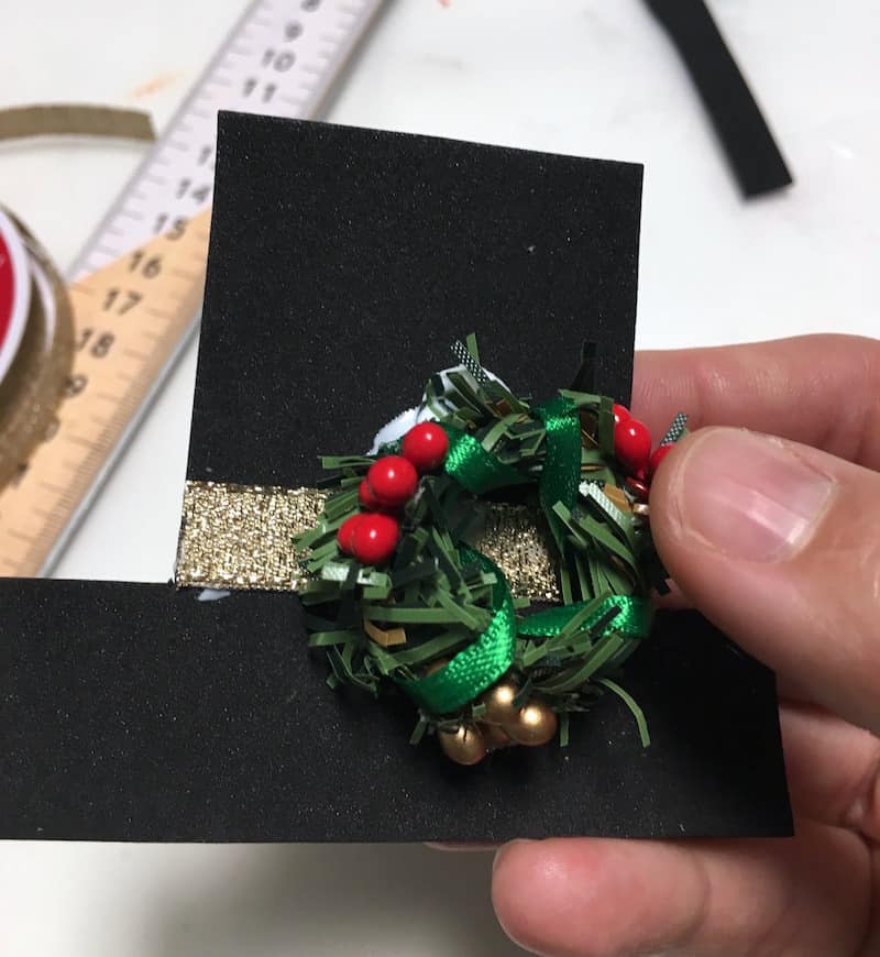 Gluing a mini Christmas wreath onto a snowman hat cut out of craft foam