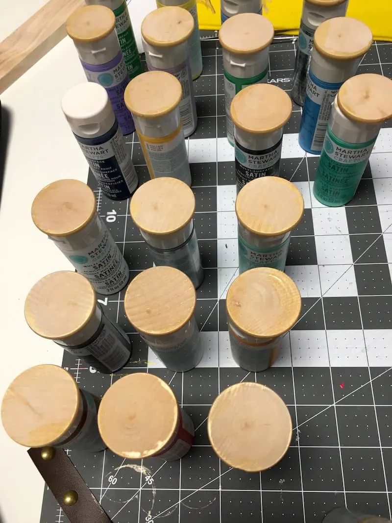 Wood circles with the edges painted in gold drying on the tops of paint bottles