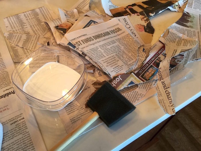 Container of Mod Podge, foam brush, and torn up pieces of newspaper