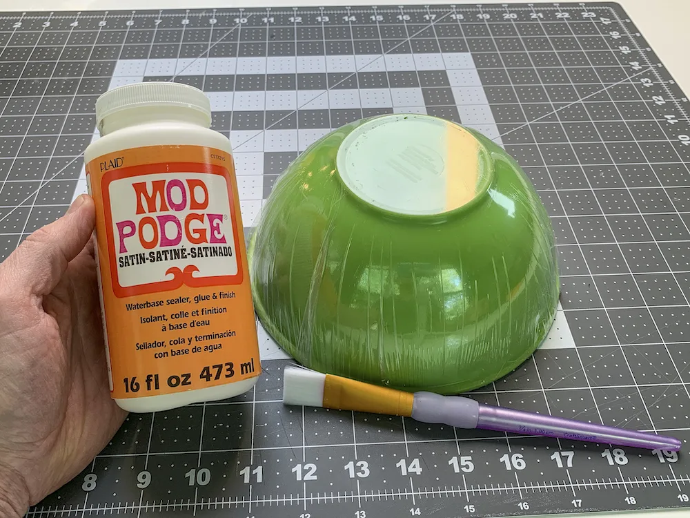 Bottle of Mod Podge Satin next to a bowl wrapped in plastic wrap with a paintbrush