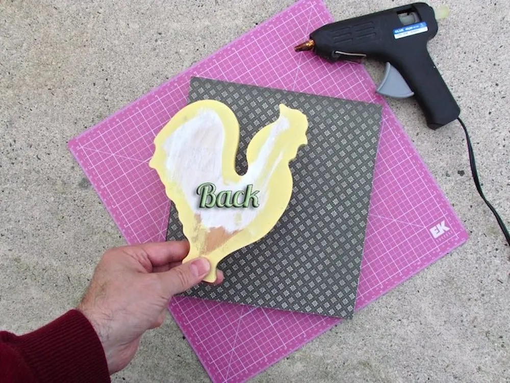 Glue a wood rooster to a wood background using a hot glue gun