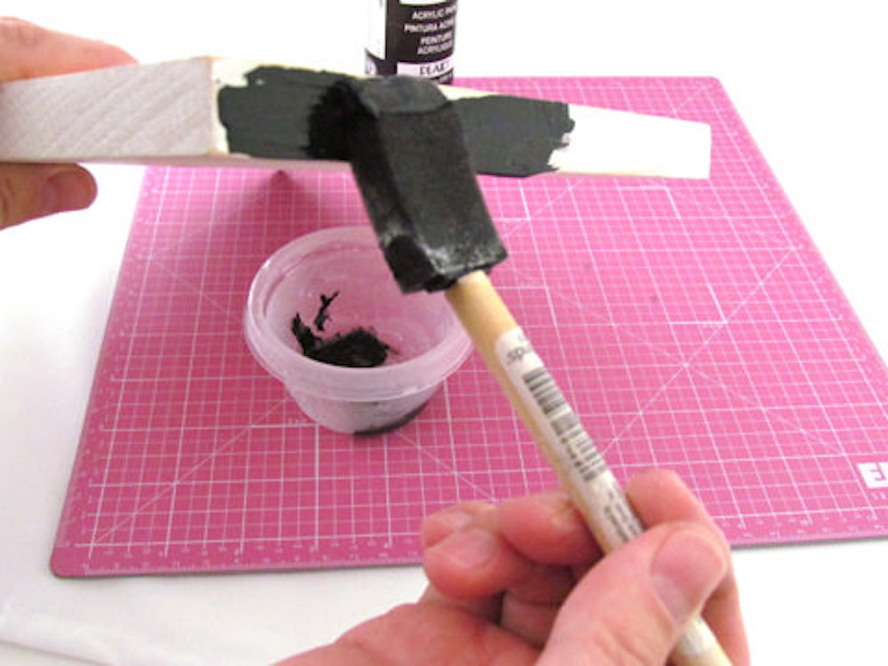 Painting the side of a piece of wood with black craft paint using a foam brush