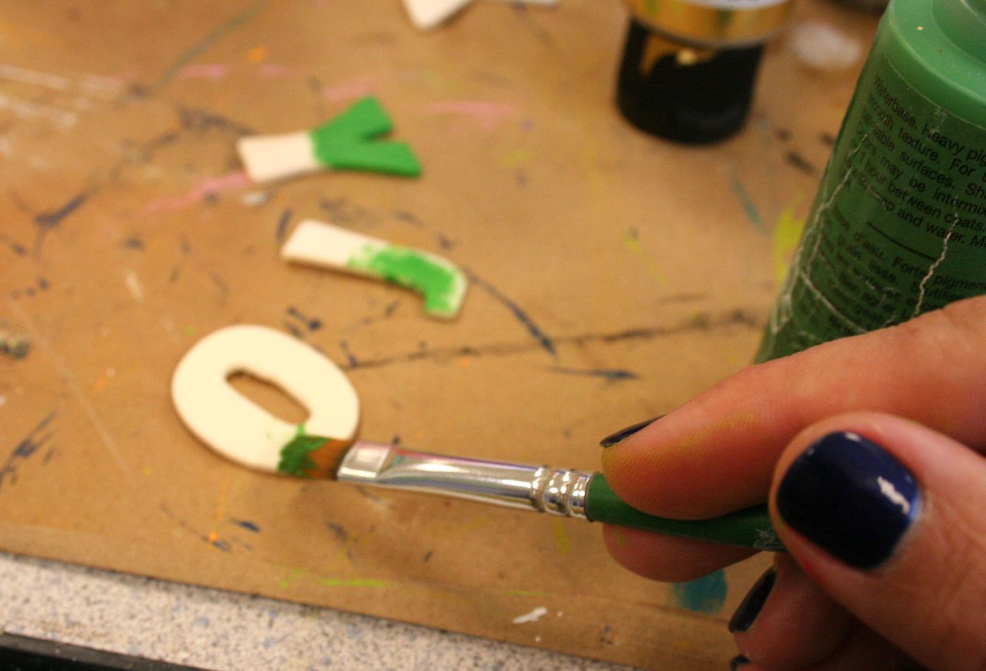 Painting wood letters that spell JOY with green acrylic paint