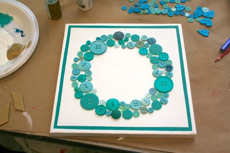 Buttons laid out in a circle wreath pattern on top of a canvas