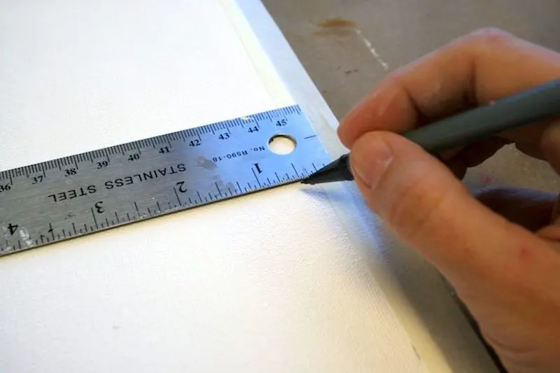 Using a ruler and a pencil to mark a board around the canvas