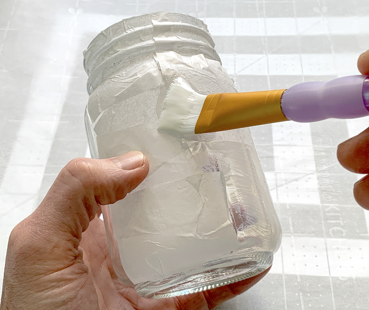 Applying Mod Podge over tissue paper on a mason jar
