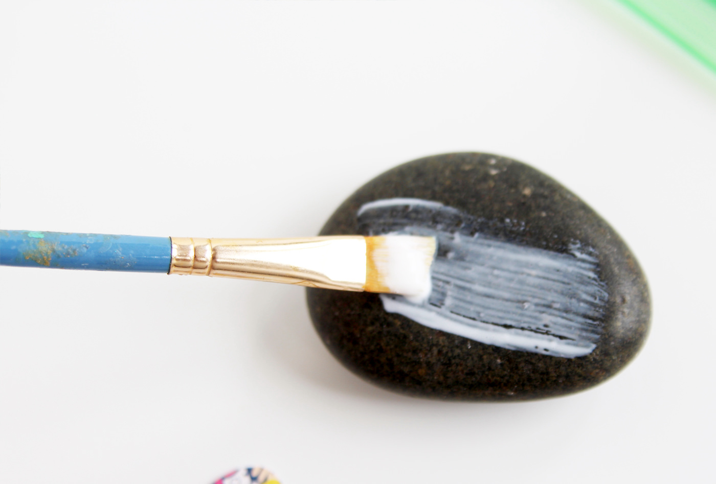 Applying a thin layer of Mod Podge to a rock with a paintbrush