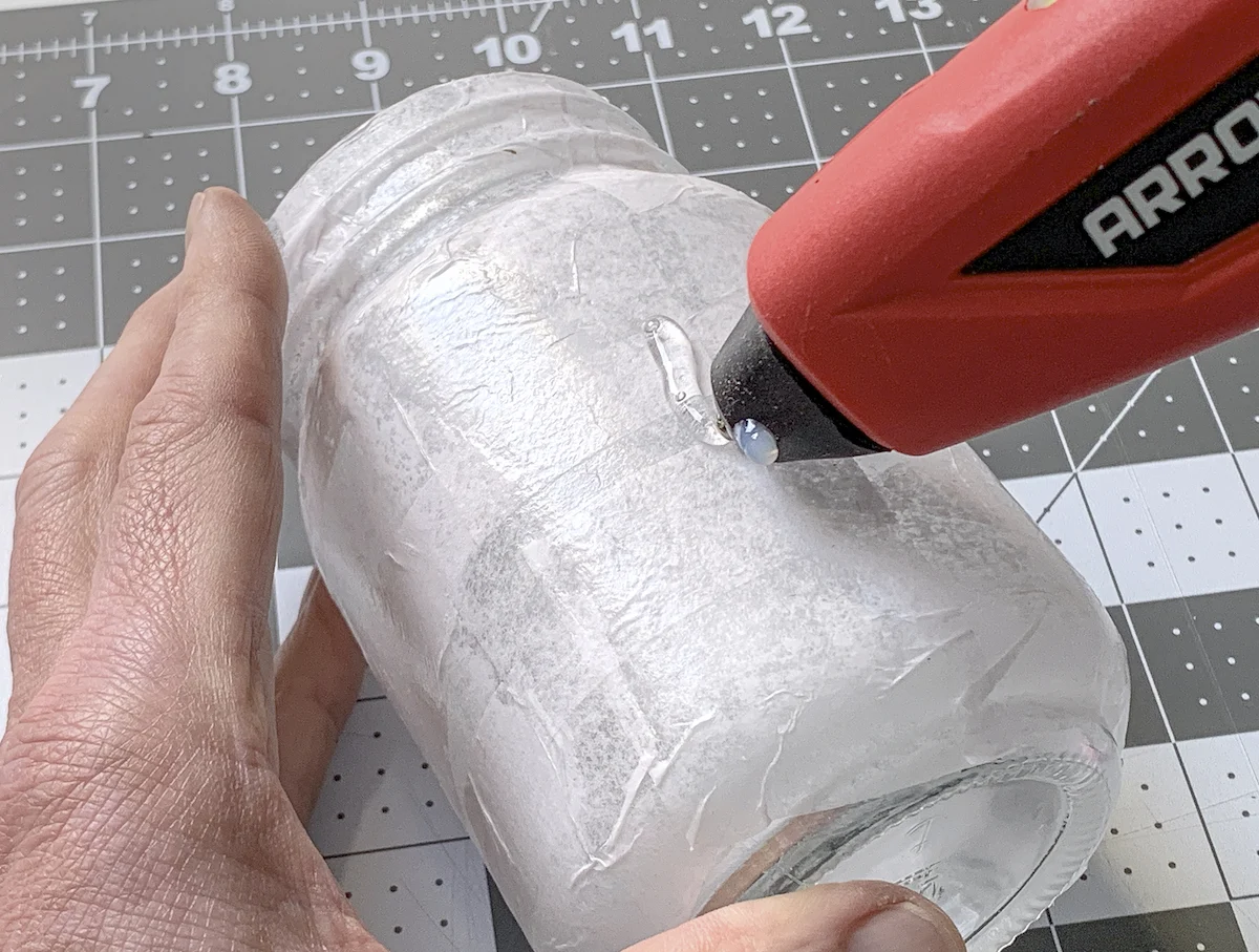 Applying hot glue to the side of a mason jar iwth a glue gun