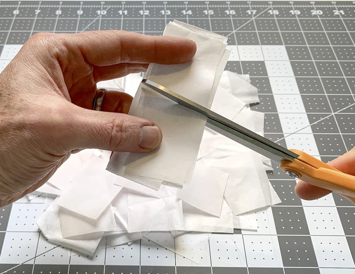 Cutting white tissue paper into squares with scissors