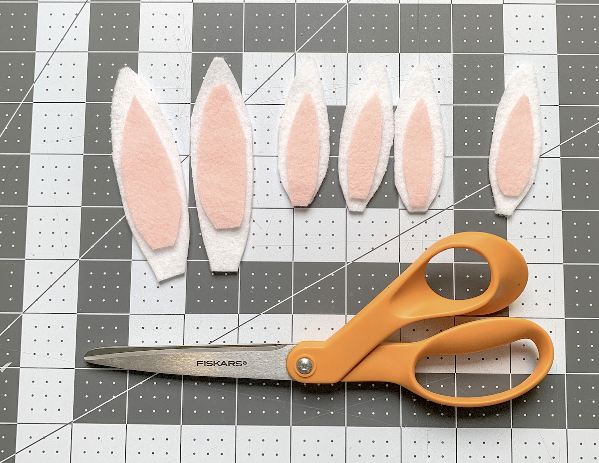 White felt bunny ears with pink centers and a pair of scissors on a craft mat